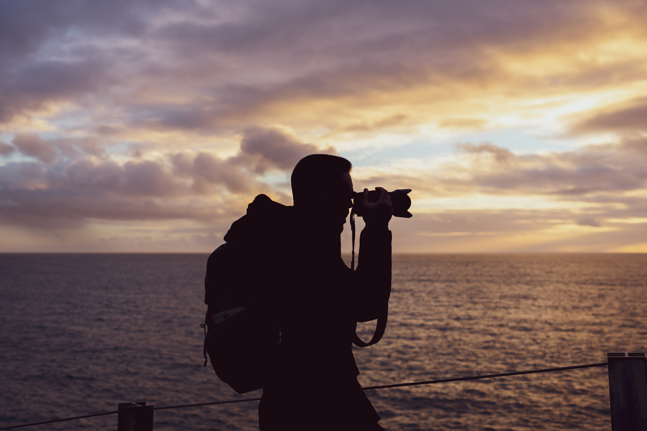 ALT Text: a person taking a picture of the ocean with the sun setting