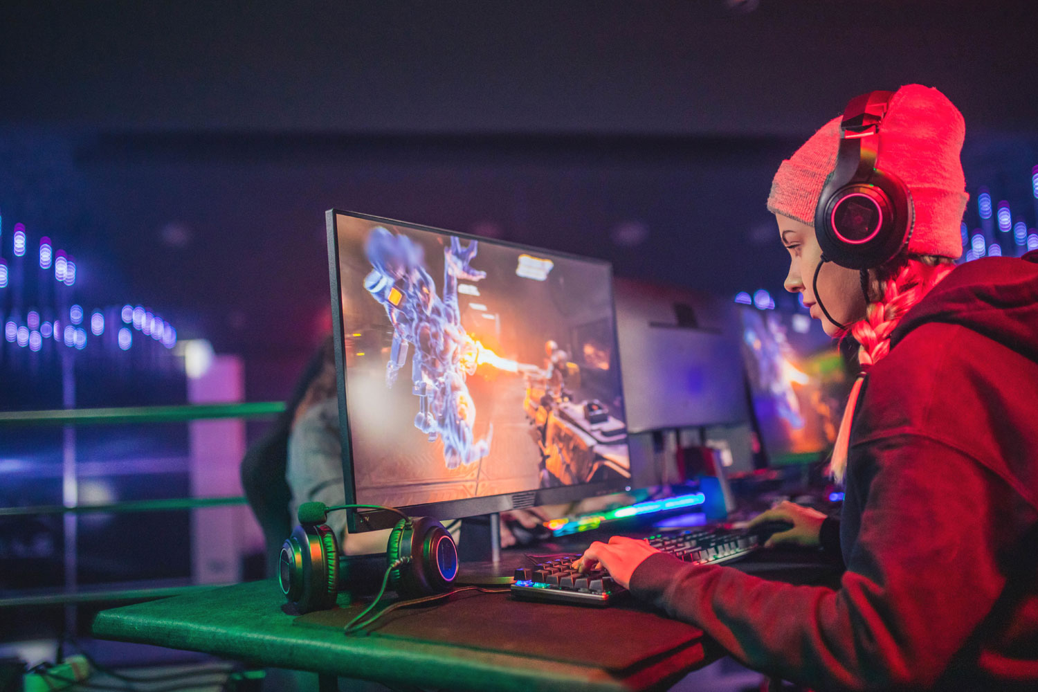 Alt Text: A woman gamer playing on a PC with LED lights set up with her Headset on 