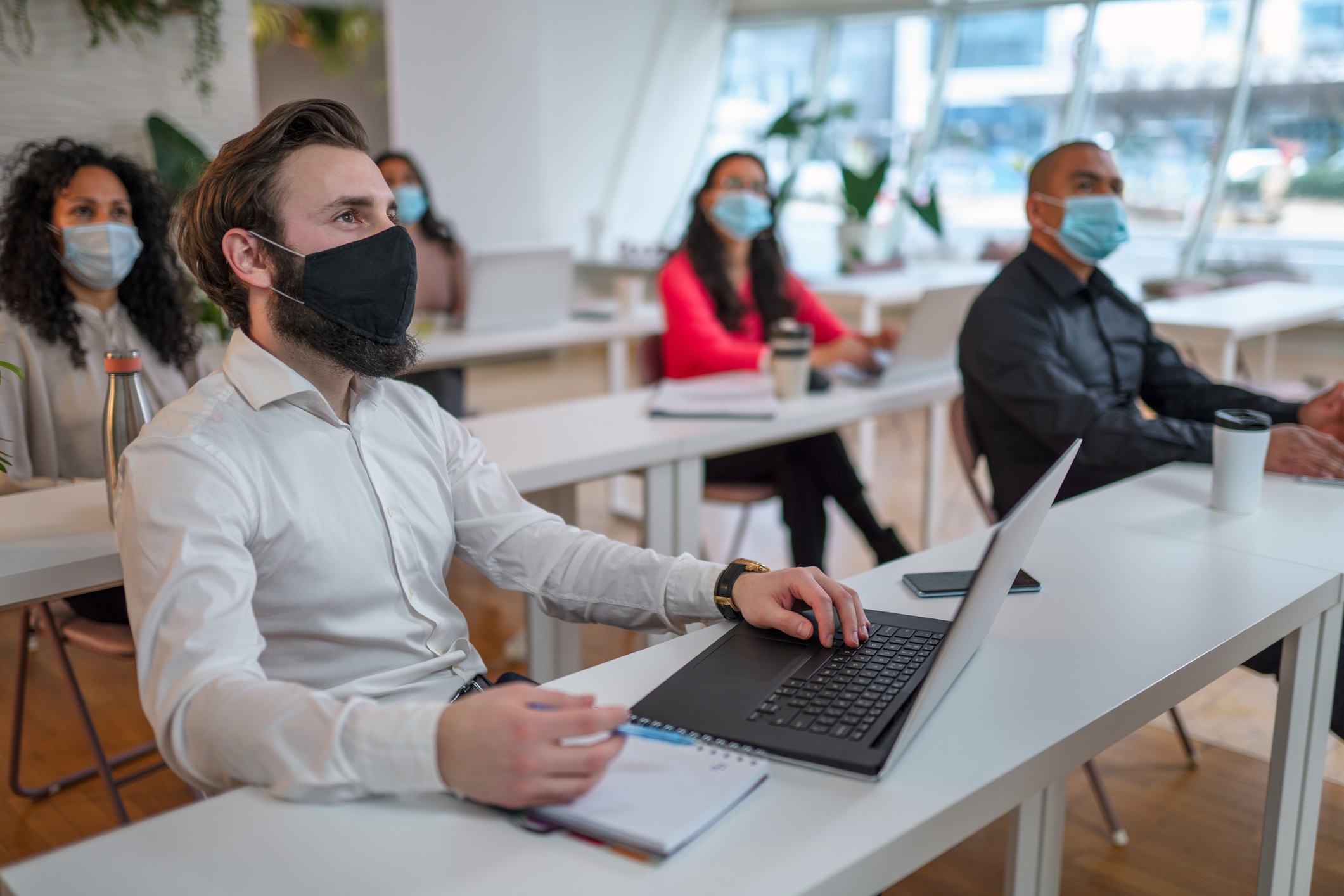 ALT Text: A conference room full of people, social distancing and wearing face masks during Covid and getting work done 