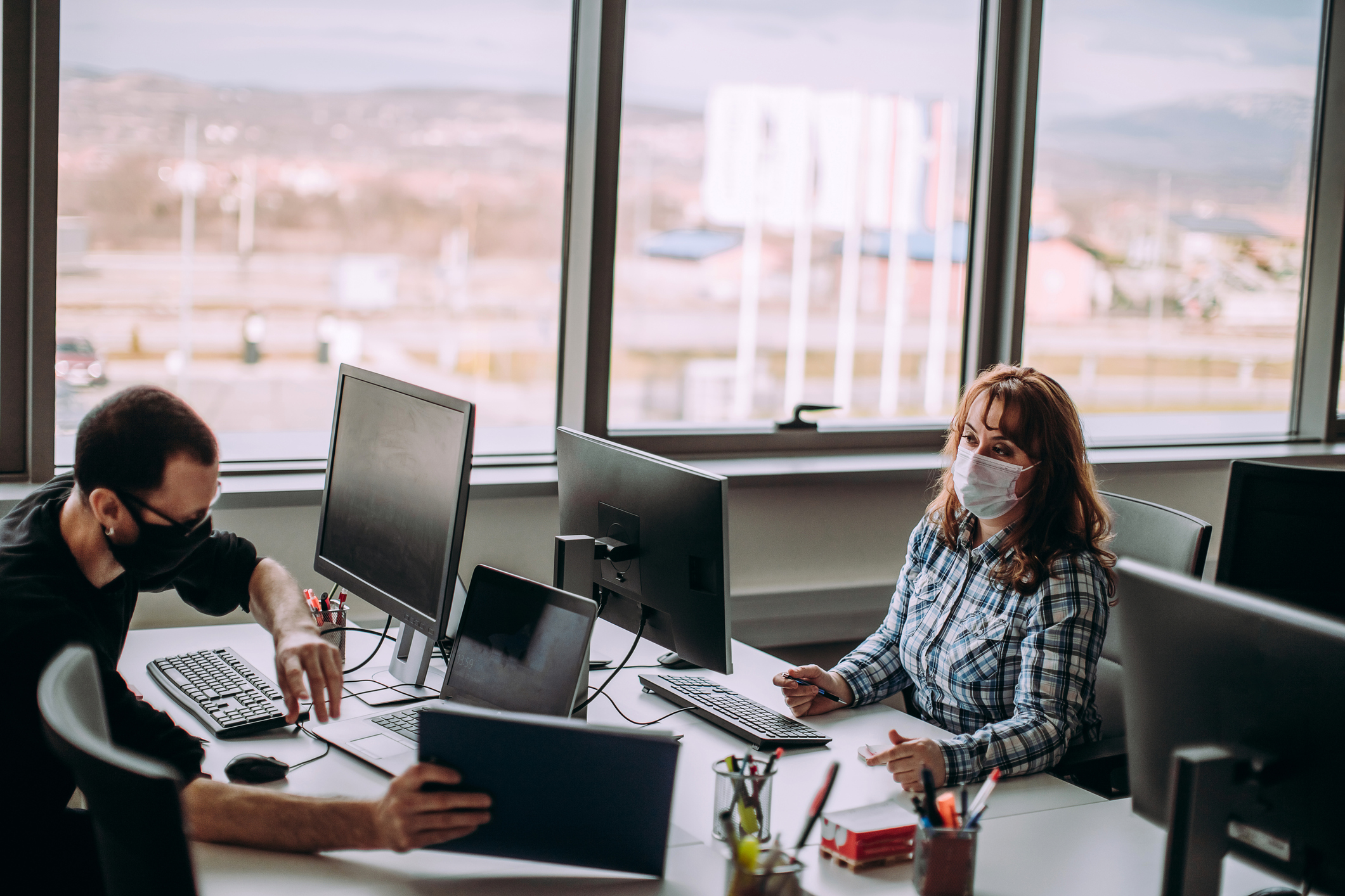 ALT Text: Two people a man and a woman working together in an office while social distancing because of covid 
