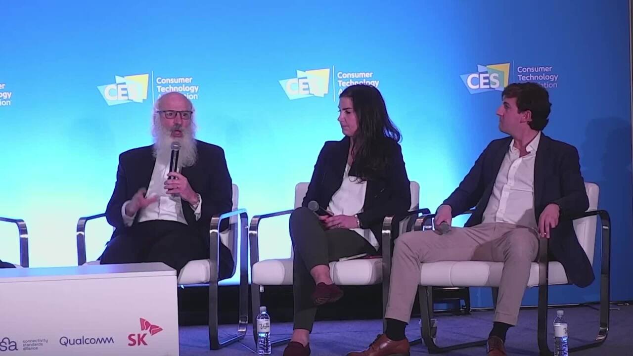 ALT Text: 3 people sitting up on stage at CES talking about what they do. with one of them having a mic.